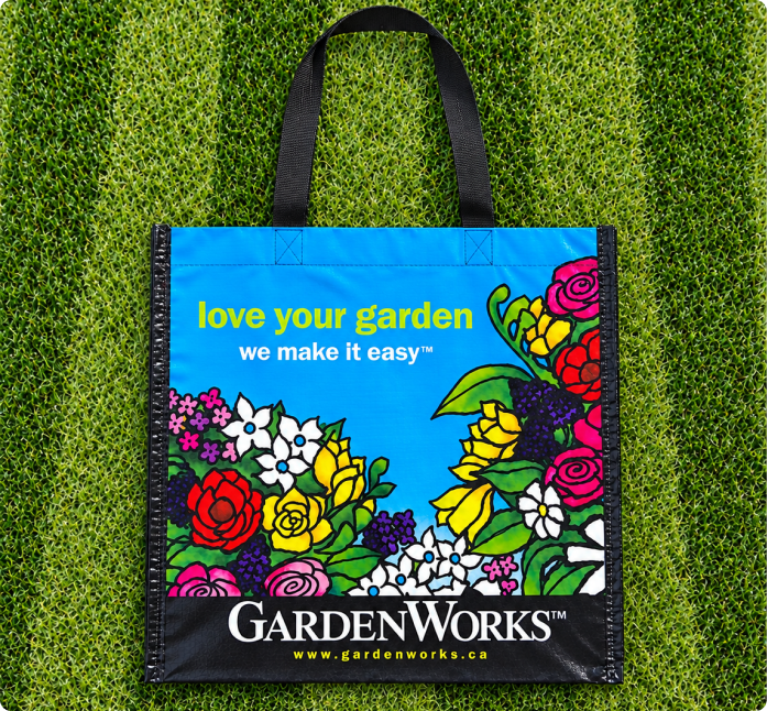 Colourful GardenWorks reusable woven shopping bag with black handles on a grass wall